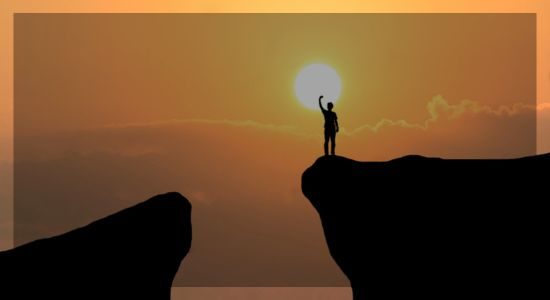 Silhouette of a person standing on a mountain peak at sunrise, symbolizing achievement, clarity, and peak performance.