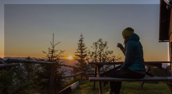 Woman sitting on a bench with a cup of coffee, watching the sunrise — symbolizing mindfulness and awakening.